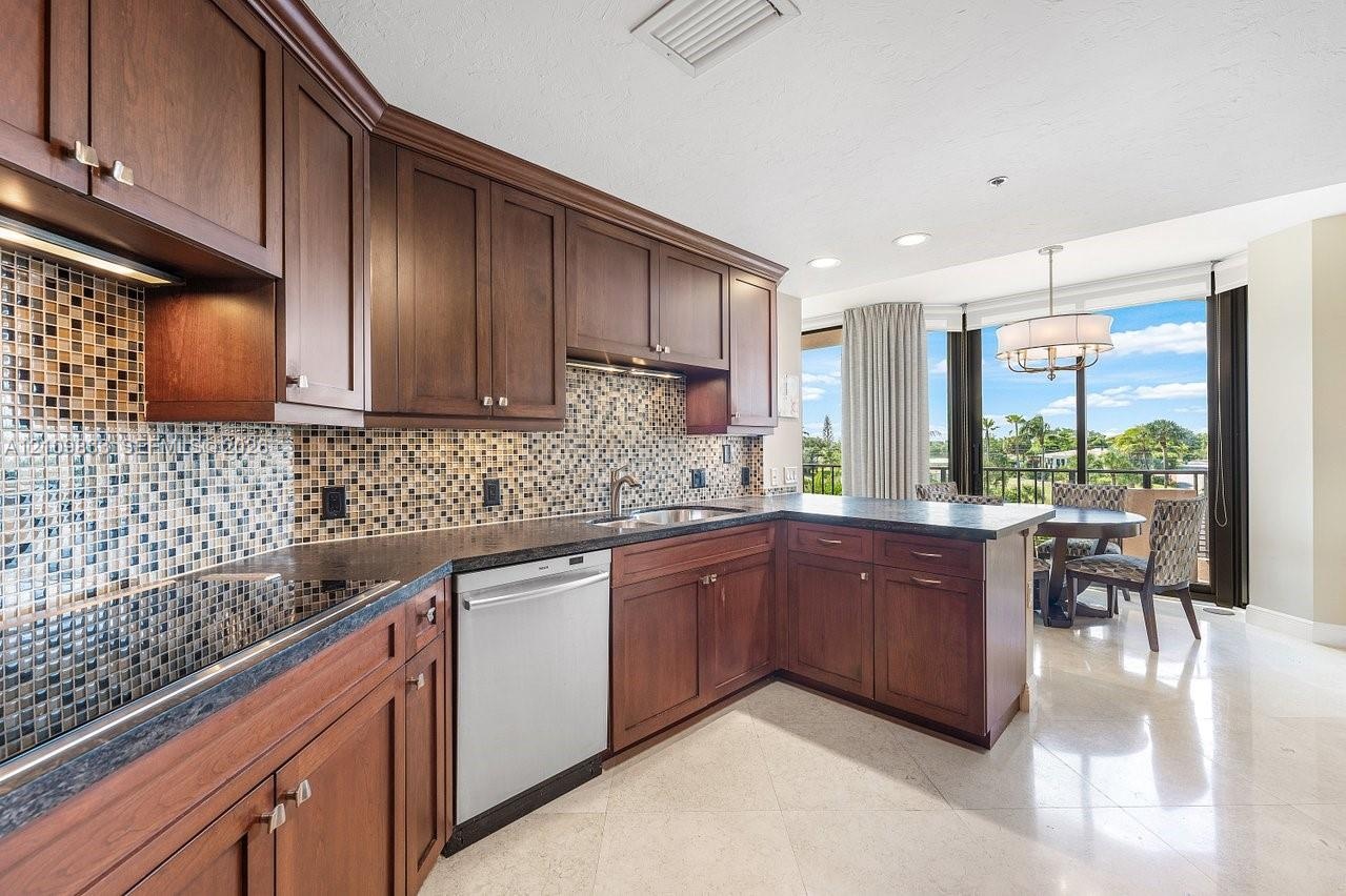 Kitchen featuring dark wood cabinetry, a mosaic tile backsplash, solid surface countertops, stainless steel dishwasher, and polished stone flooring