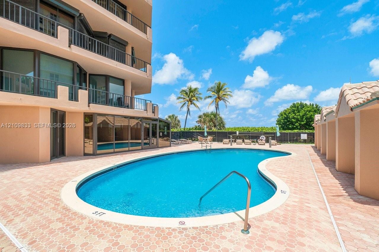 Swimming pool with a curved concrete deck, metal handrail, perimeter privacy fencing, and exterior balconies