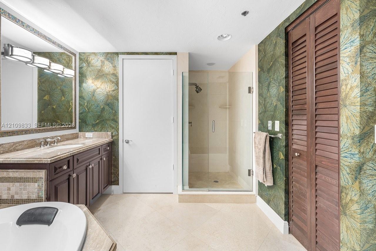 Bathroom featuring a dark wood-finish vanity with a stone countertop, an oversized wall mirror with decorative trim, a walk-in glass-enclosed shower, 