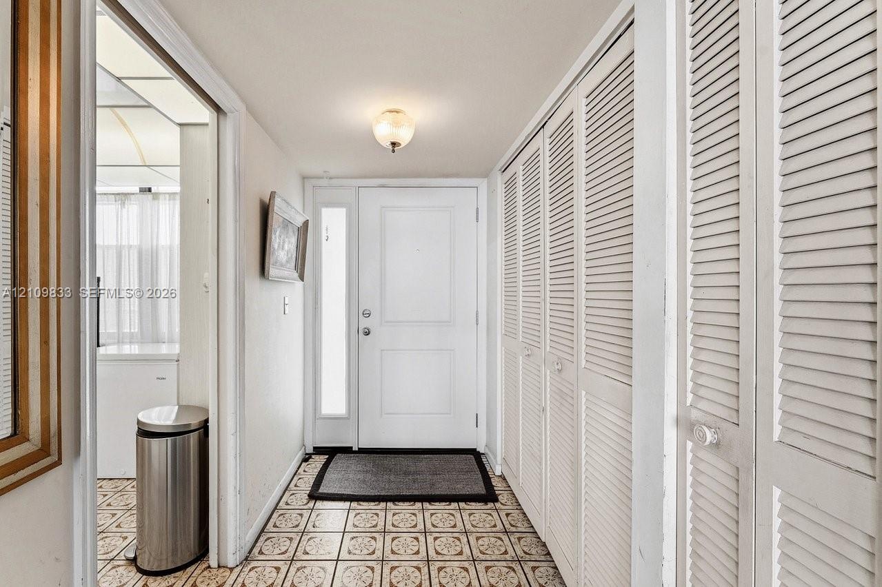 Entryway featuring a white paneled door with a vertical glass sidelight, floor-to-ceiling white louvered-style closet doors, patterned tile flooring, 