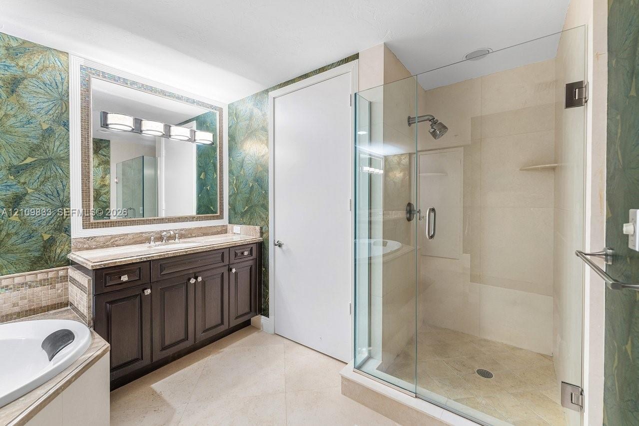 Dark wood cabinetry with stone-finish vanity top, glass-enclosed shower with tile surround, large-format tile flooring, and integrated soaking tub