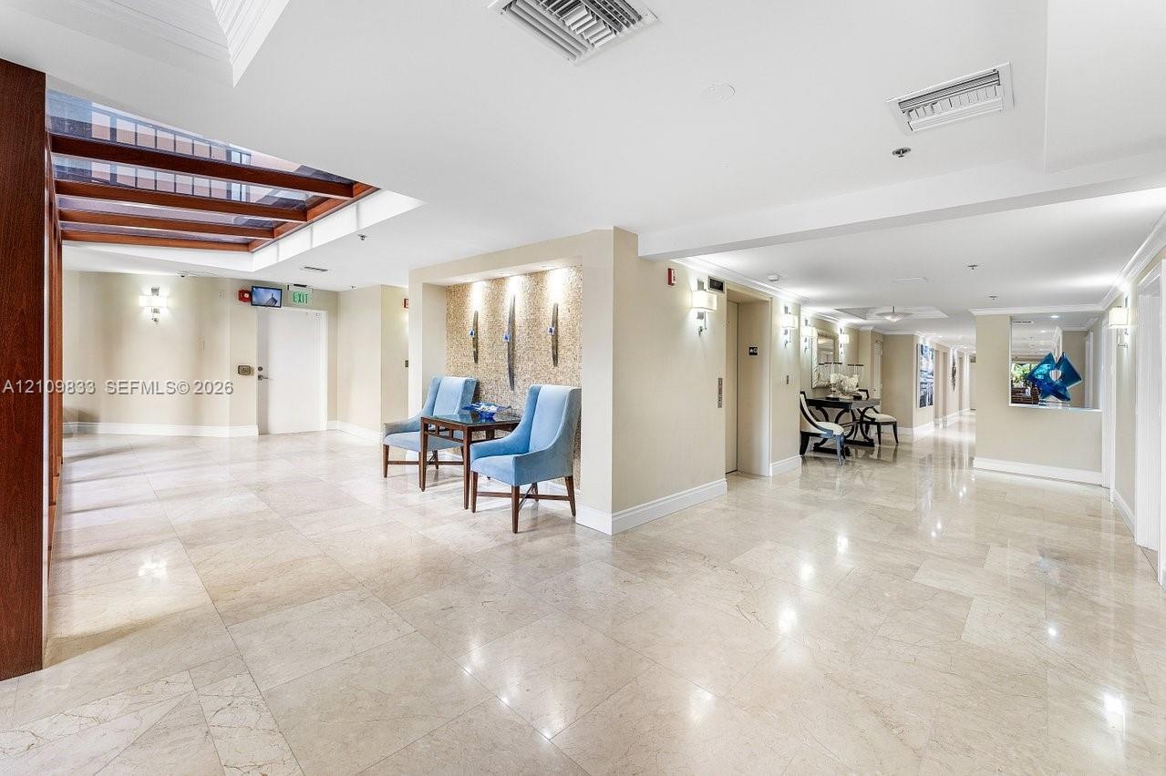 Spacious lobby featuring polished stone flooring, recessed ceiling lighting, a wood-beam architectural detail, and a decorative alcove with vertical w