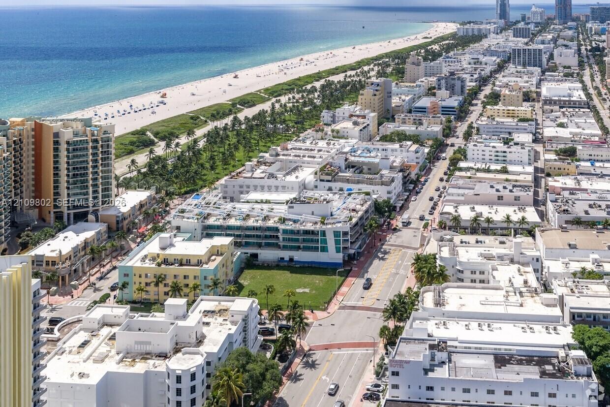 Aerial perspective of a coastal urban district featuring proximity to an expansive shoreline, dense multi-story architecture, and established palm tre