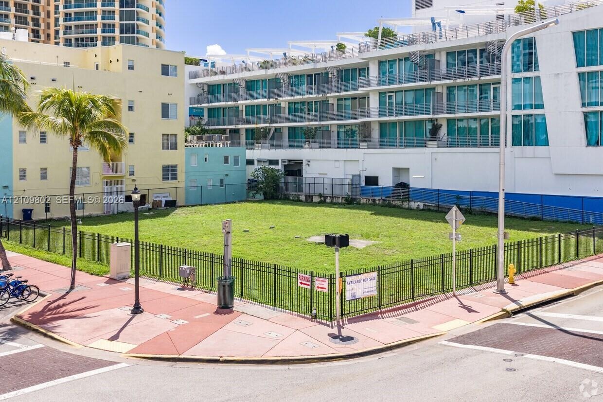 Cleared corner lot enclosed by black metal fencing, featuring level terrain and an established palm tree
