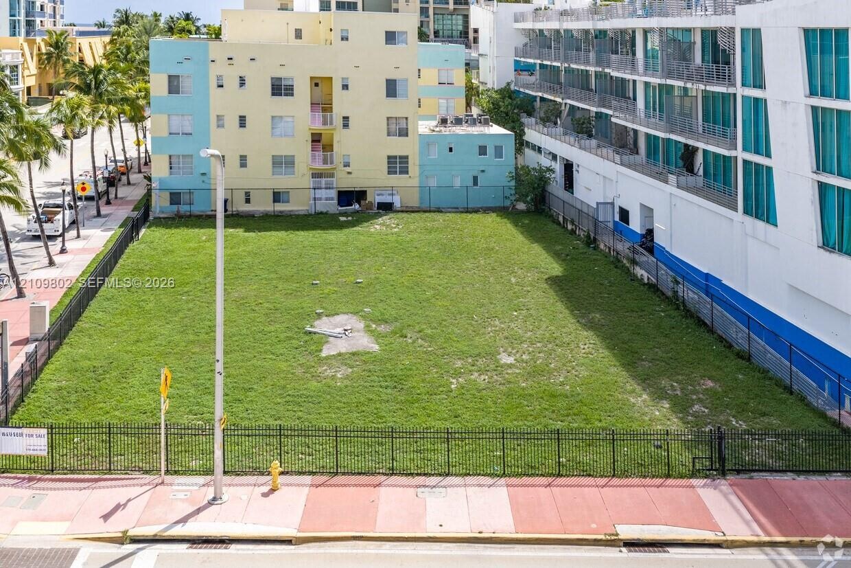 Rectangular urban parcel enclosed by perimeter metal fencing with direct street access and sidewalk frontage