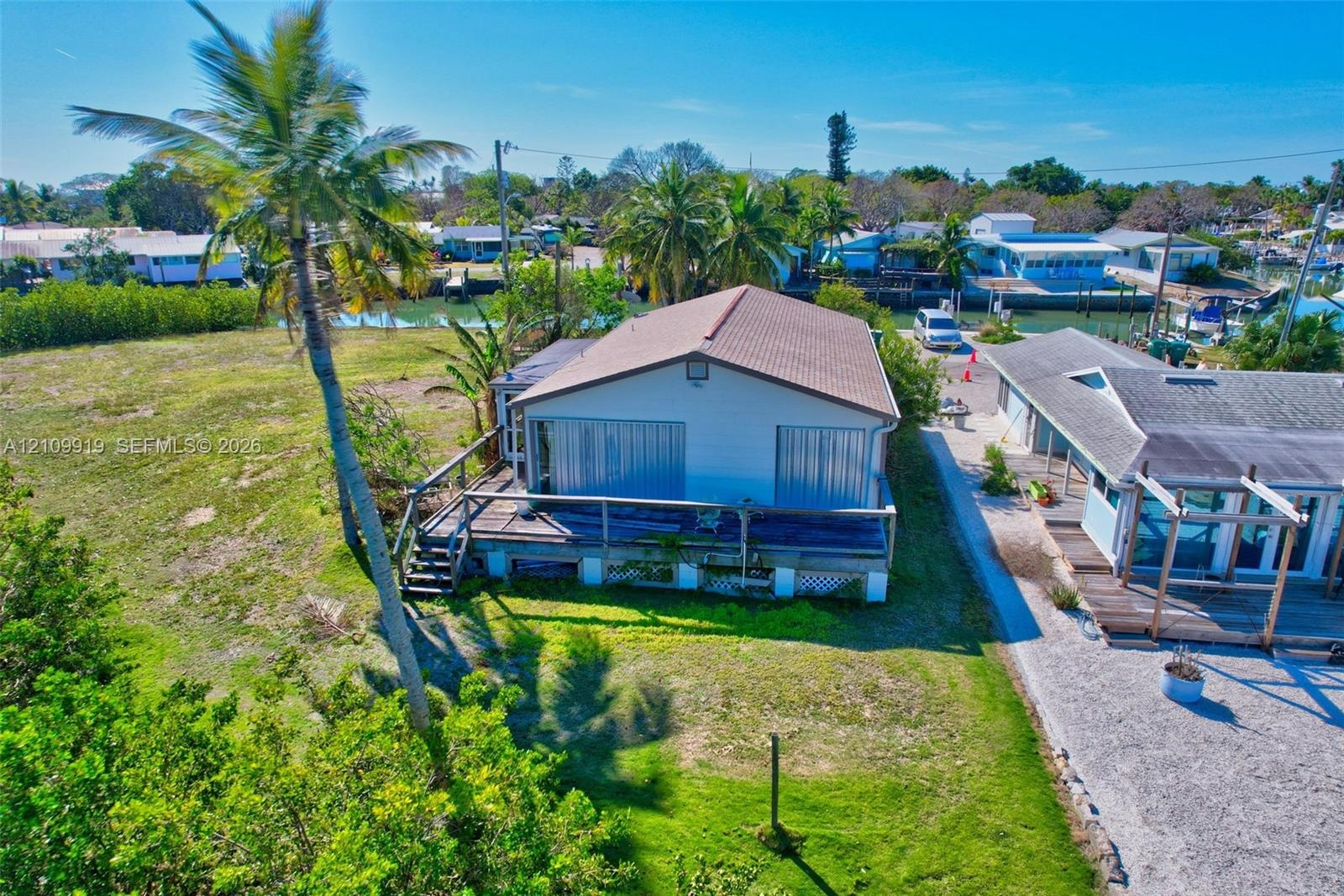 Waterfront property featuring a wood deck, structural pier, expansive lawn, and mature palm trees
