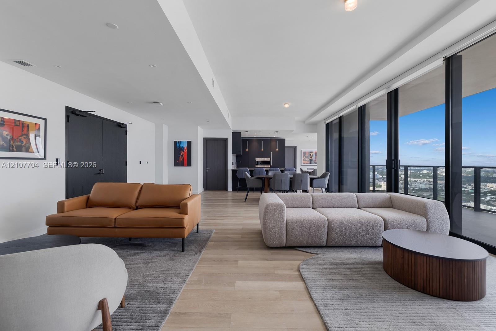 Open-concept living space featuring wood-finish flooring, floor-to-ceiling glass wall, recessed lighting, and kitchen cabinetry with integrated applia