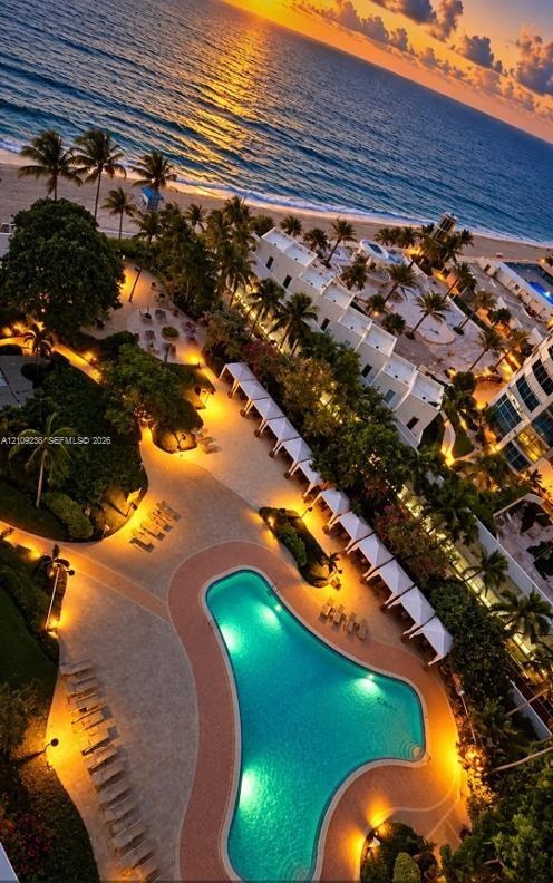 Aerial perspective of coastal property featuring an expansive swimming pool with hardscaped surround, multiple cabanas, mature palm trees, and direct 
