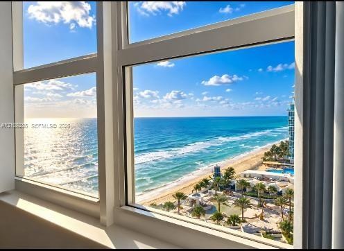 Floor-to-ceiling windows with white frames, showcasing coastal scenery including an expansive ocean and sand shoreline