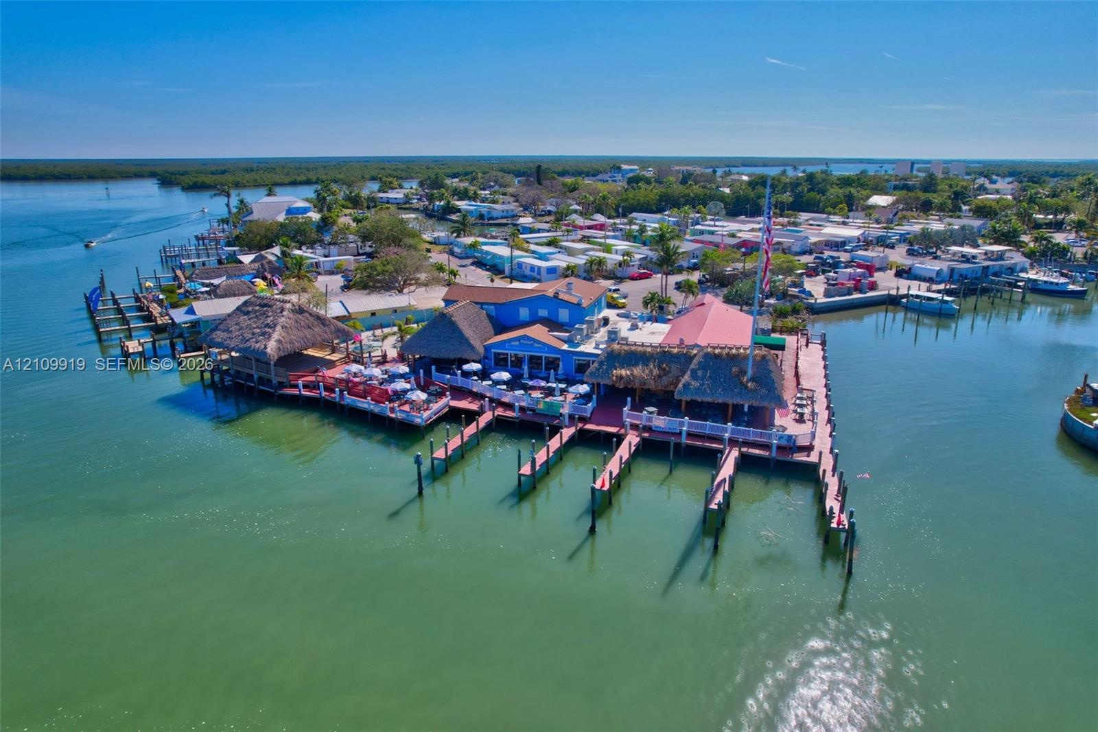 Waterfront property featuring multiple boat slips, thatch-roofed outdoor covered pavilions, and expansive wood-plank decking