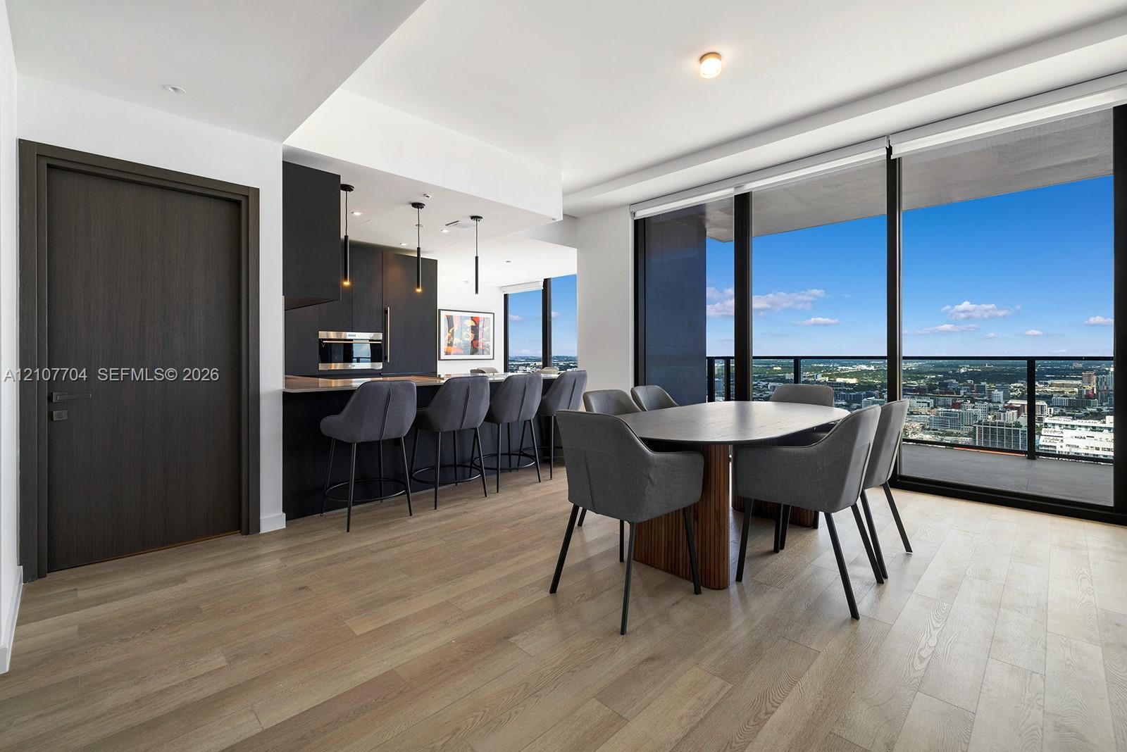Open-concept interior featuring light wood-finish flooring, floor-to-ceiling windows, matte black cabinetry, built-in stainless steel appliances, and 