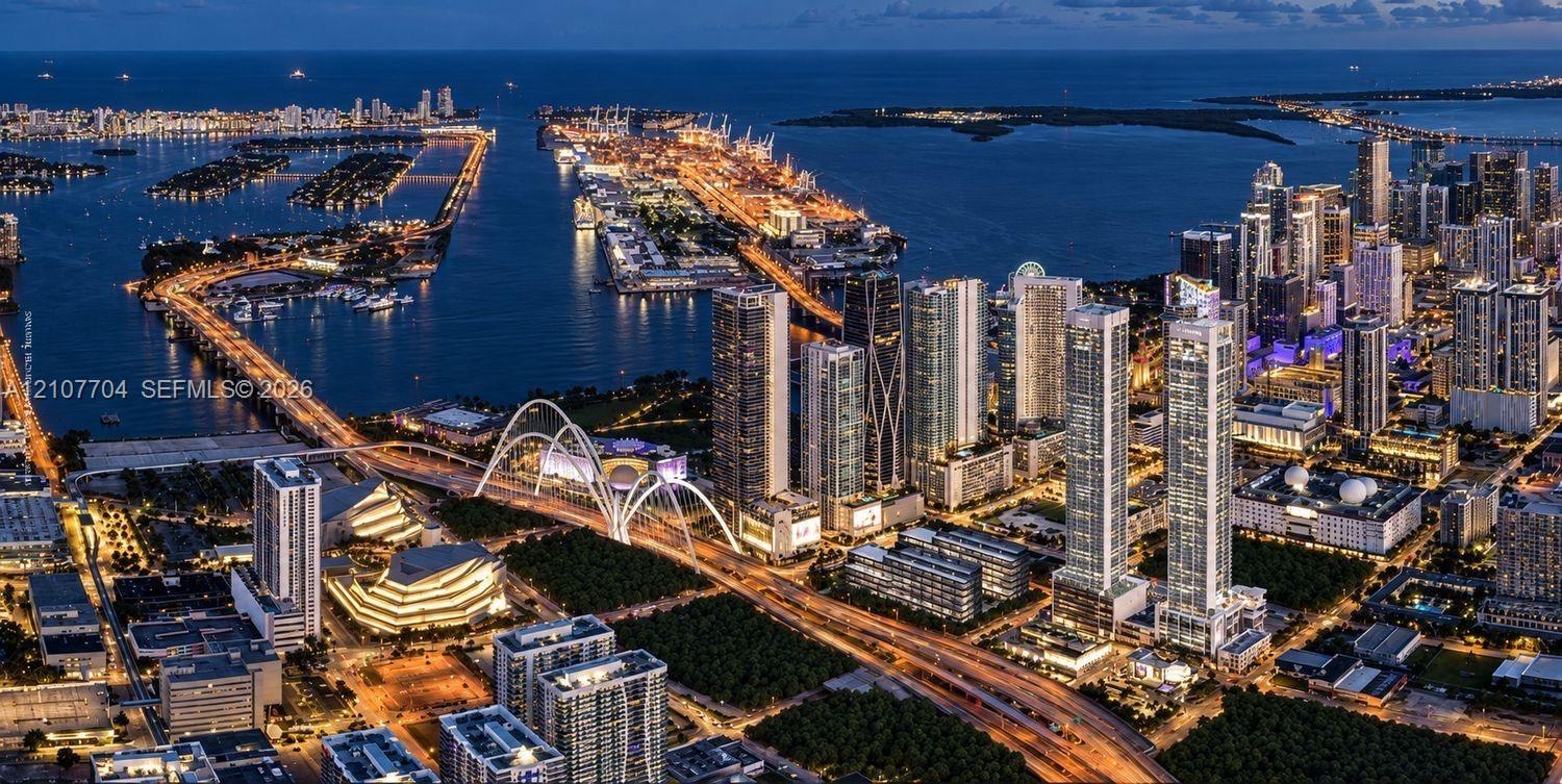 Aerial perspective of a metropolitan skyline featuring high-rise architecture, proximity to a coastal waterway, complex bridge infrastructure, and den