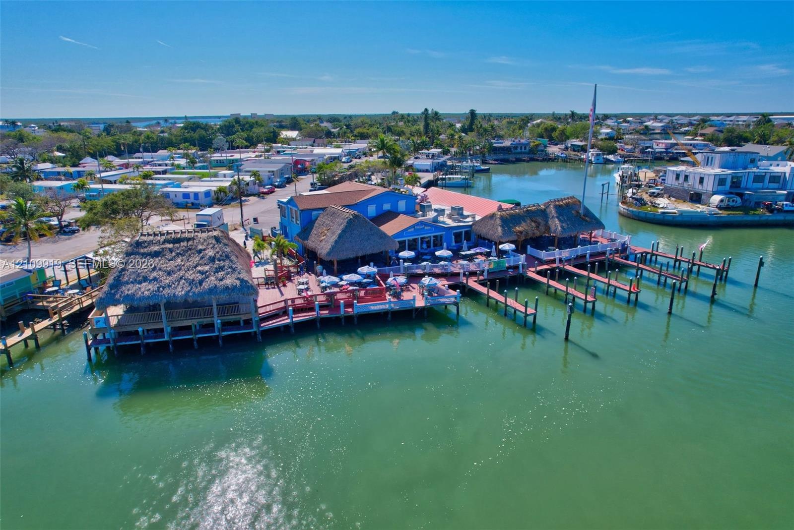 Waterfront commercial property featuring multiple thatched-roof structures, expansive wooden deck space, and private boat slips