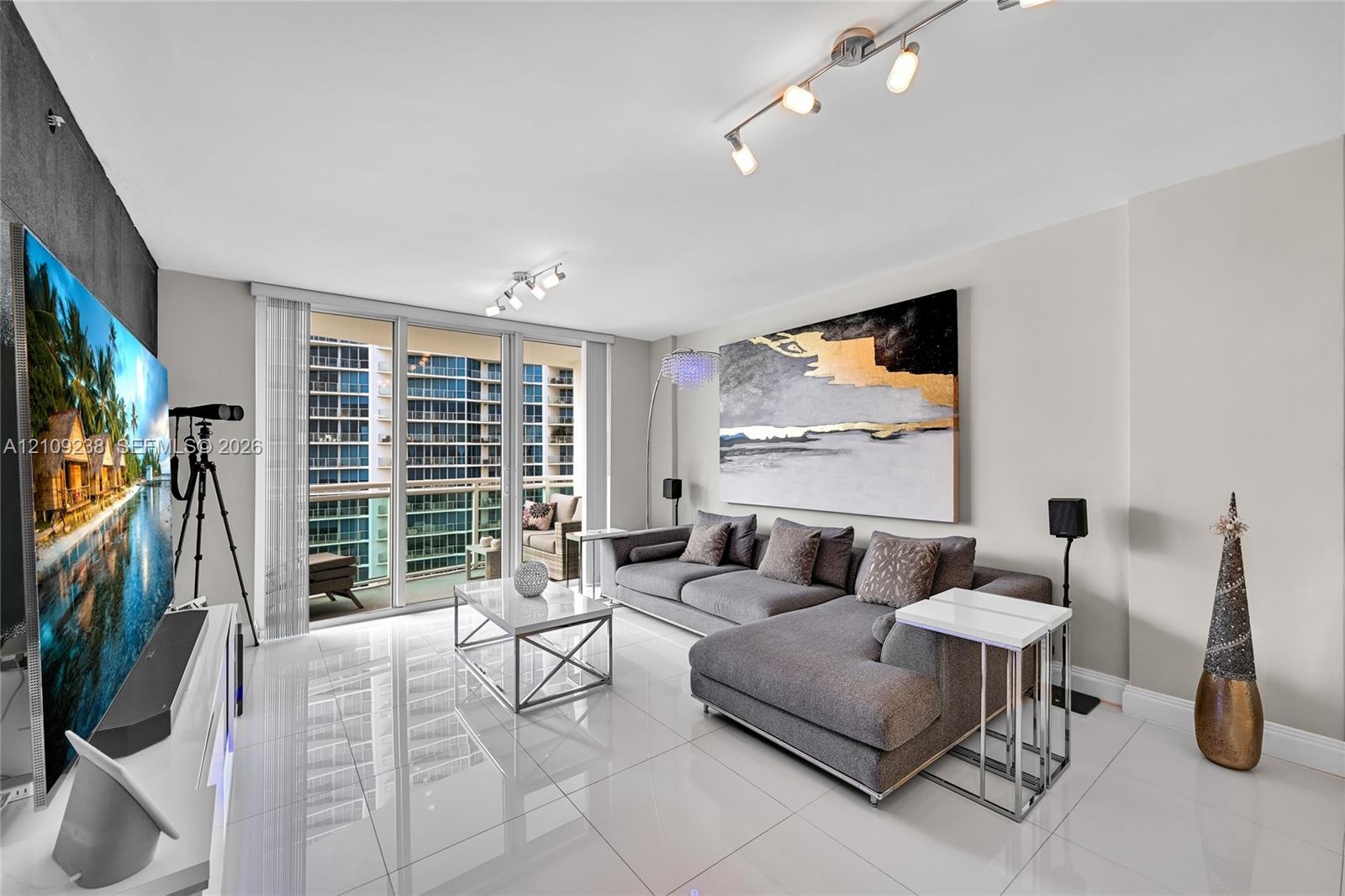 Large-format tile flooring, floor-to-ceiling glass sliding doors, private balcony, and multi-directional track lighting