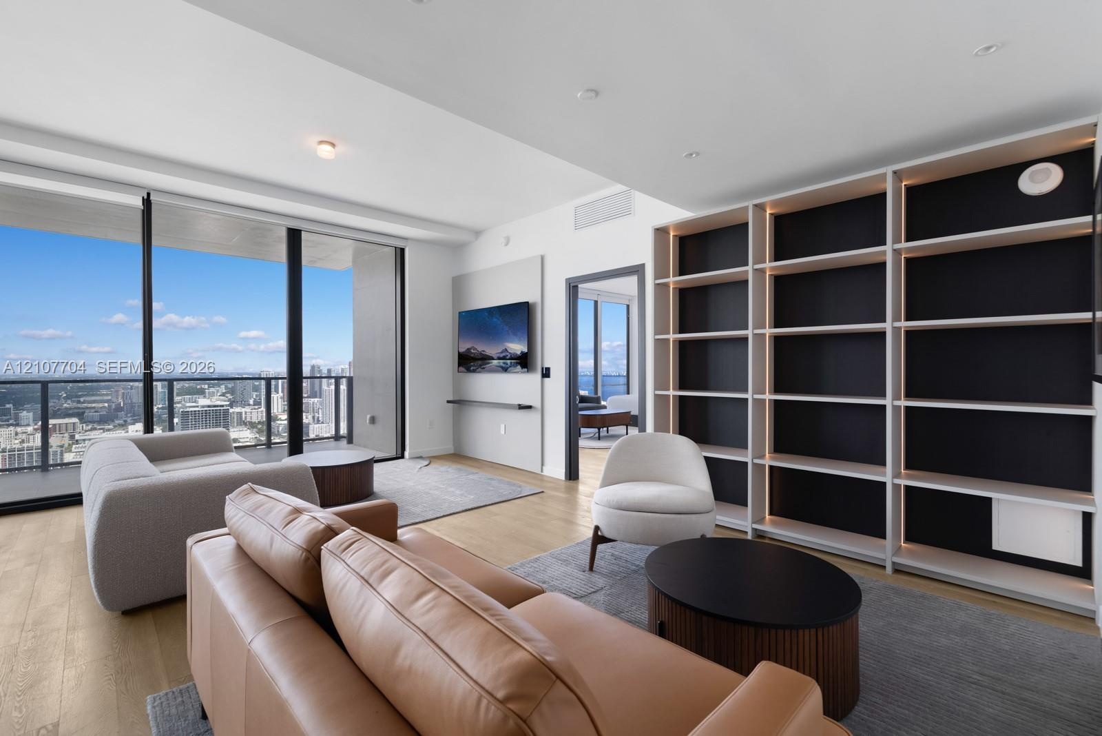 Floor-to-ceiling glass windows, wide-plank wood-finish flooring, custom built-in shelving with integrated lighting, and a private balcony