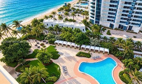 Oceanfront grounds featuring a swimming pool, multiple poolside cabanas, manicured landscaping, and direct beach access