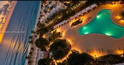 Aerial perspective of beachfront property featuring an expansive swimming pool, stone-paved pool deck, palm tree landscaping, and direct access to the
