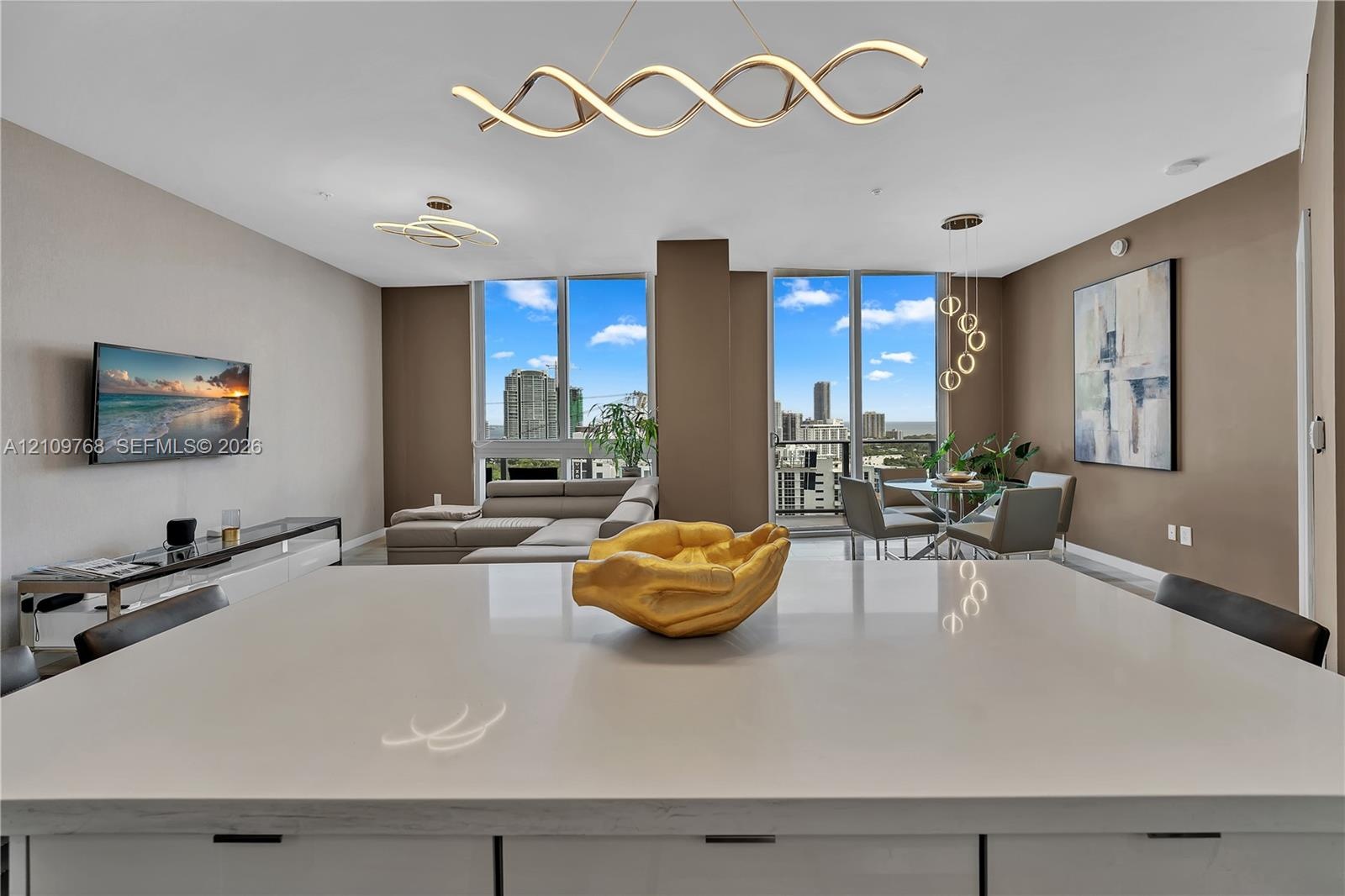 Expansive quartz island with white cabinetry, floor-to-ceiling windows, and contemporary sculptural lighting fixtures