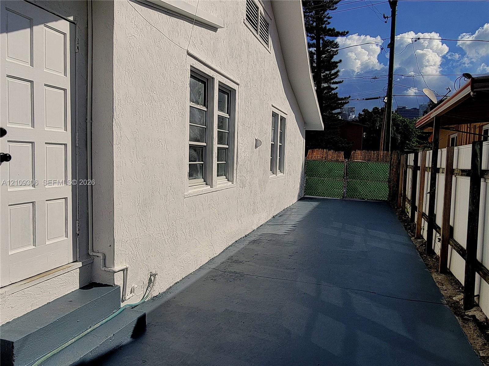 Stucco exterior featuring dual-pane windows, a solid-core exterior door, concrete surface, and perimeter fencing