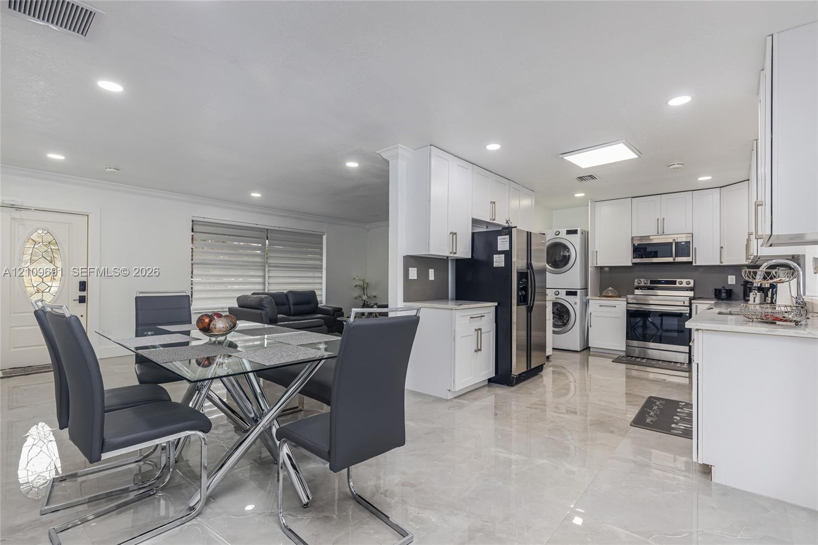 Kitchen featuring white shaker-style cabinetry, stainless steel appliances, stacked laundry unit, polished tile flooring, and recessed lighting