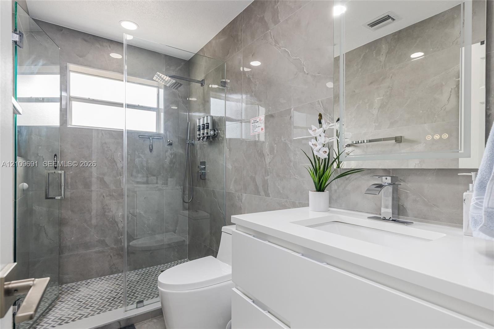 Bathroom featuring a glass-enclosed walk-in shower with floor-to-ceiling stone-finish tile, a floating white vanity with a rectangular sink, and a bui