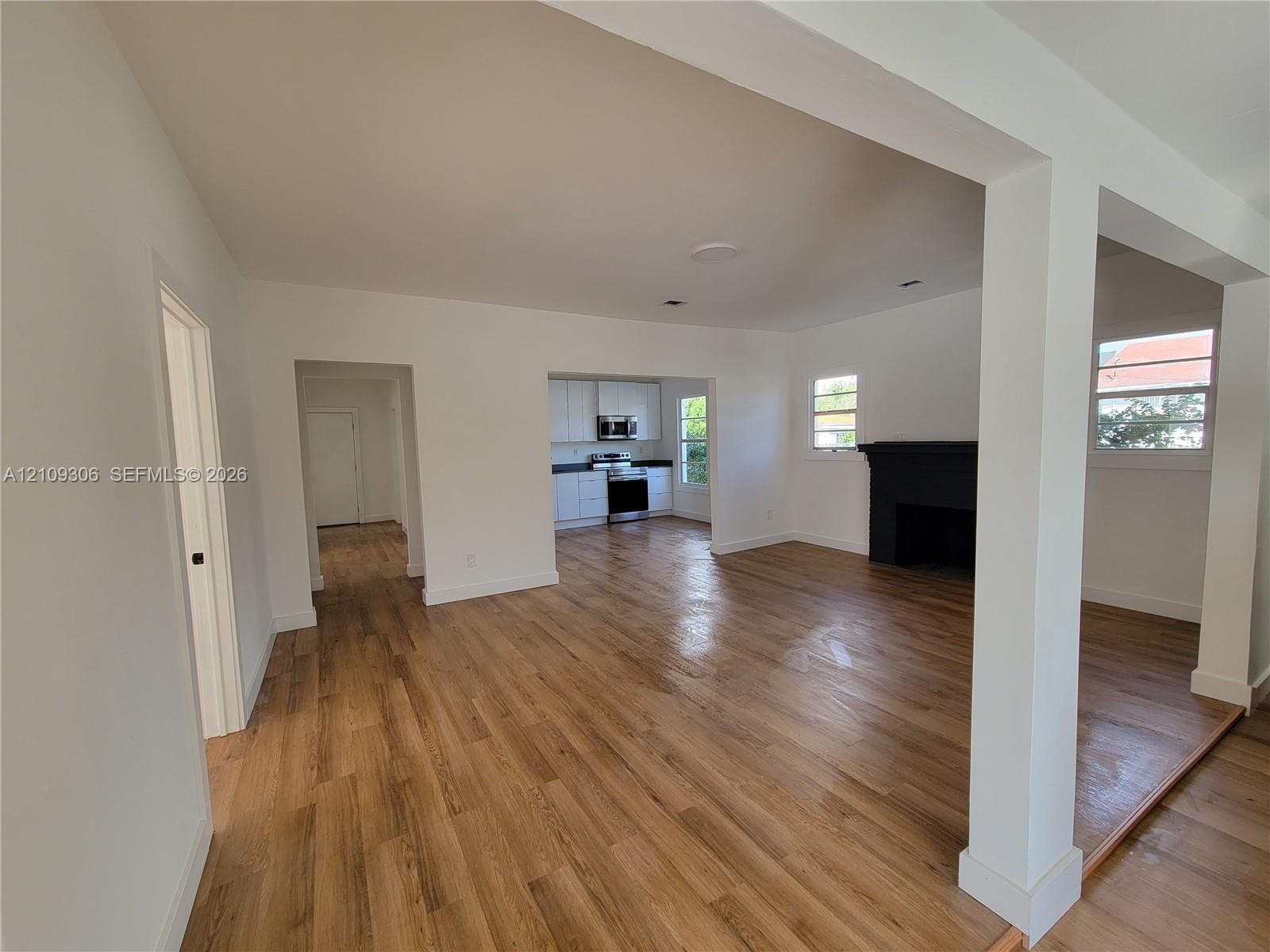 Open living space featuring wood-finish flooring, a painted brick fireplace, and kitchen cabinetry with integrated stainless steel appliances