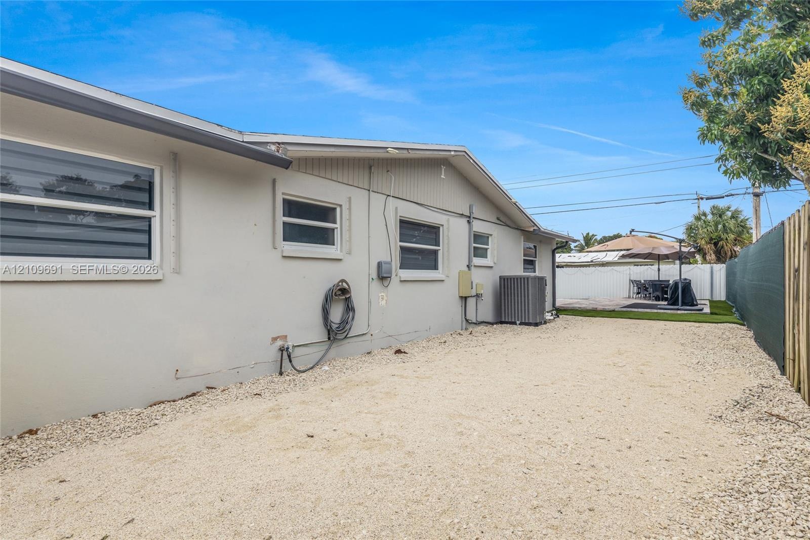 Exterior side profile featuring a light-toned stucco finish, horizontal sliding windows, gravel ground cover, and a privacy fence