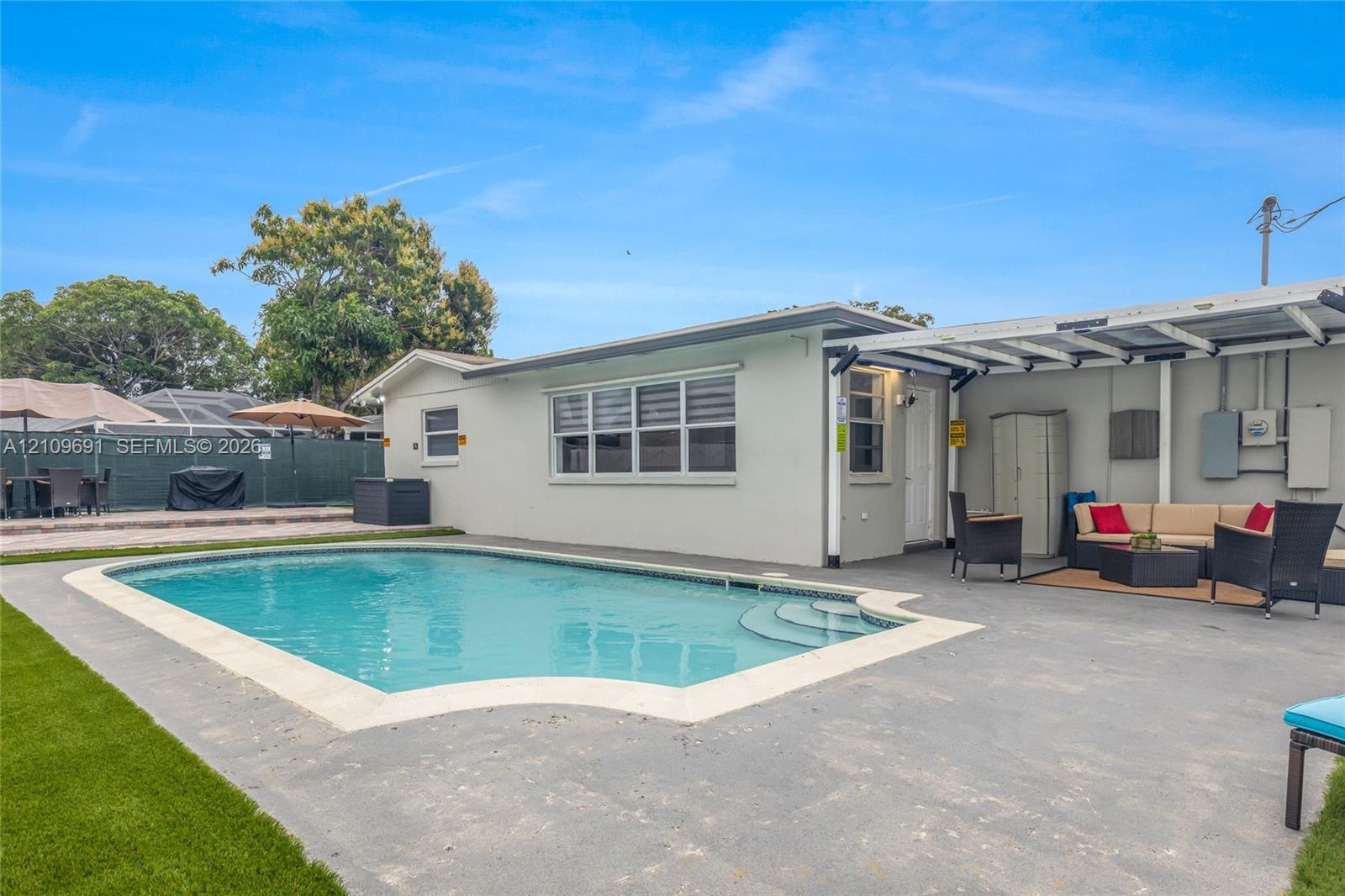In-ground swimming pool with integrated steps, concrete patio, artificial turf lawn, and covered outdoor area