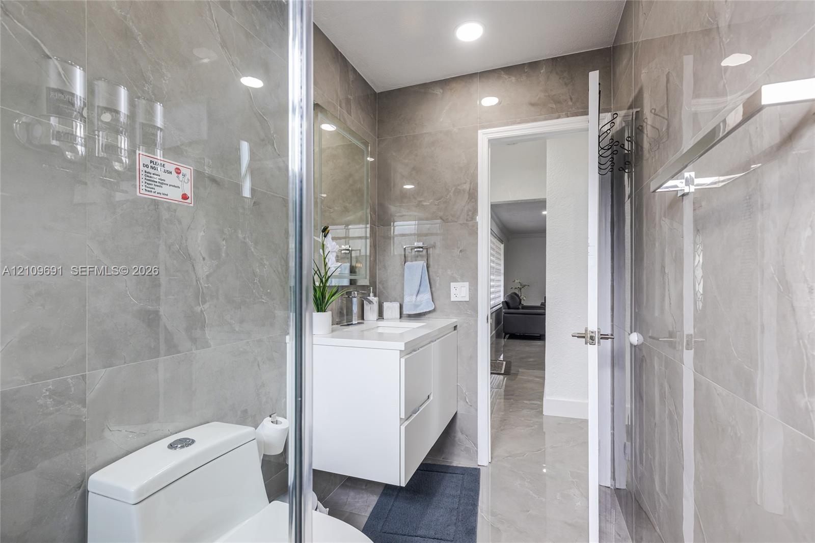 Full-height stone-finish wall tile, floating white vanity, recessed ceiling lighting, glass-enclosed shower, and polished stone-finish flooring