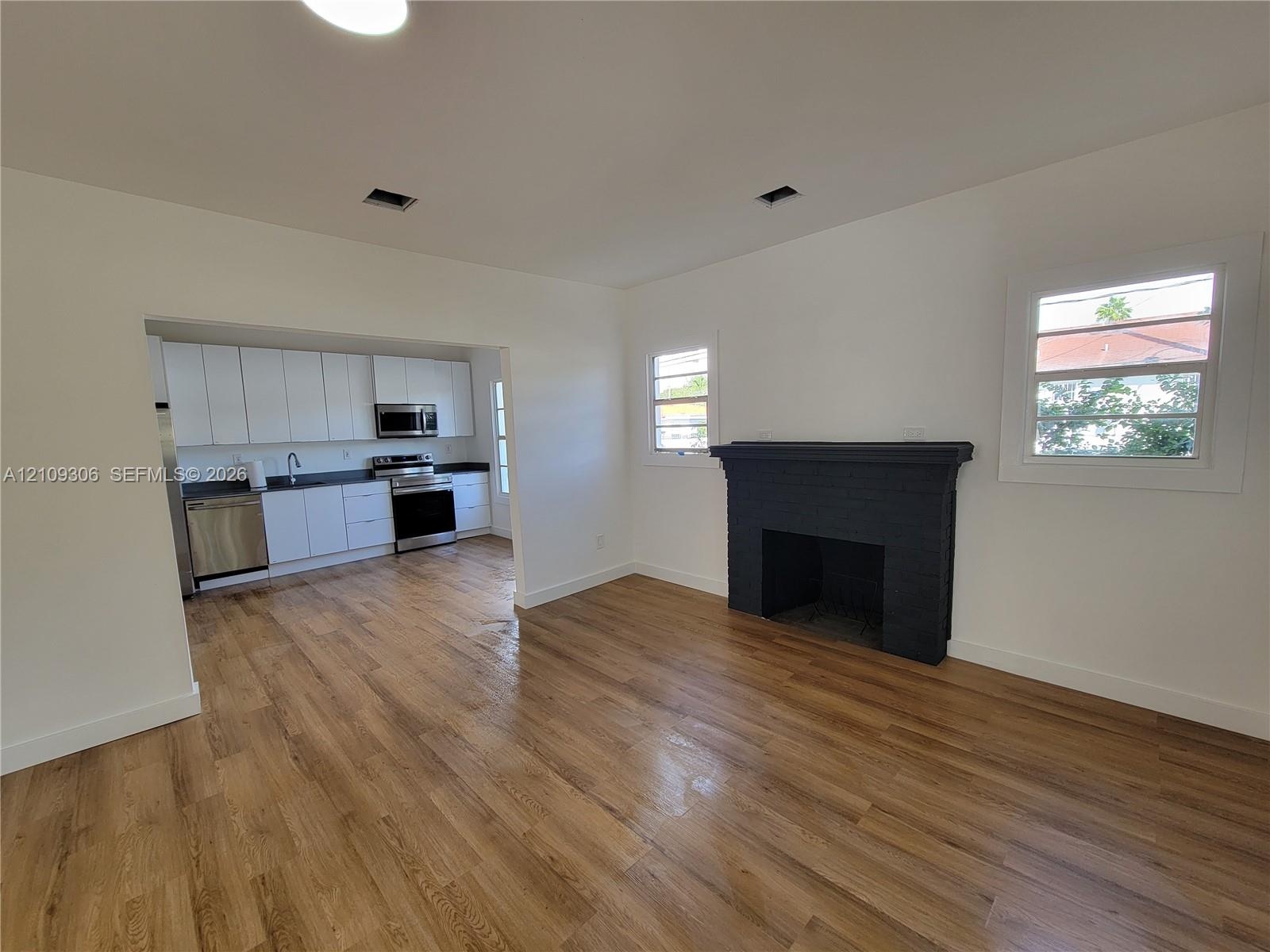 Wood-finish flooring, matte black fireplace surround, white flat-panel cabinetry, stainless steel kitchen appliances, and windows with white casings