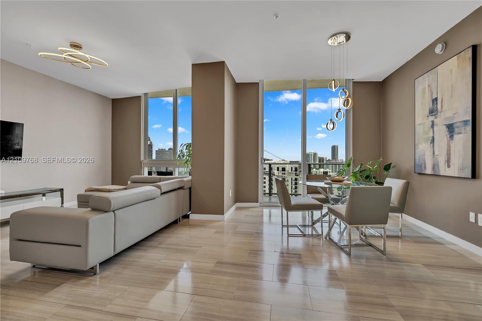Open-concept interior featuring floor-to-ceiling windows, neutral wall tones, polished stone flooring, modern geometric chandelier lighting, and a pri