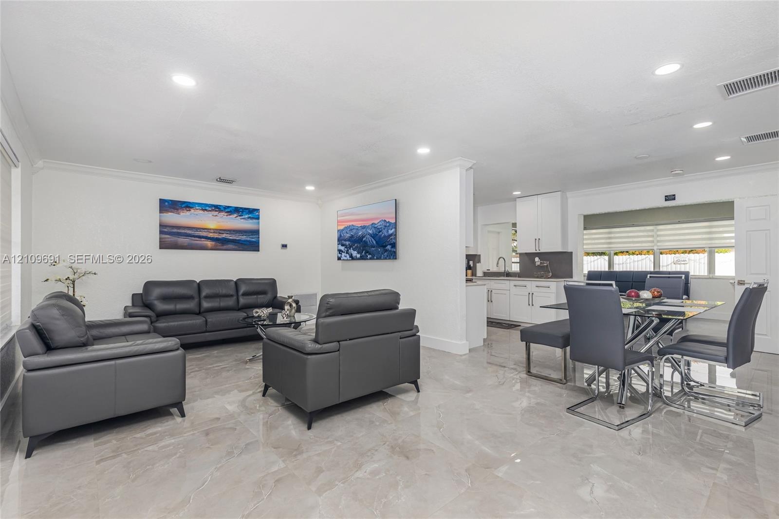 Open-concept interior featuring large-format polished tile flooring, recessed lighting, crown molding, and white shaker-style cabinetry