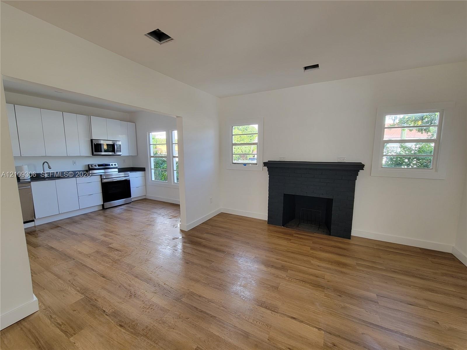 Kitchen featuring flat-panel white cabinetry, dark countertops, and stainless steel appliances, paired with wood-finish flooring and a central firepla