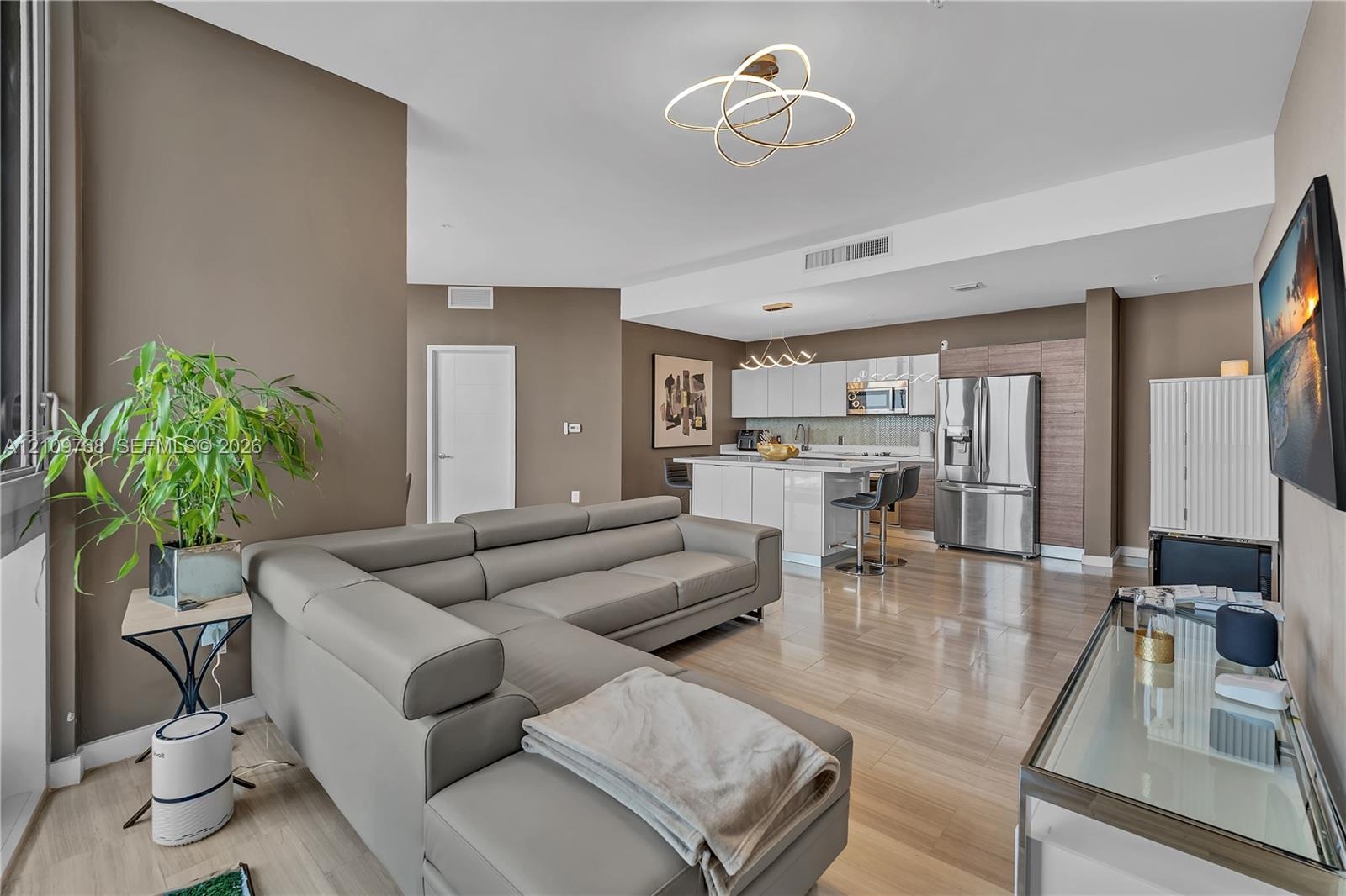 Open-concept living space featuring high-gloss cabinetry, stainless steel appliances, wood-finish flooring, and contemporary geometric light fixtures