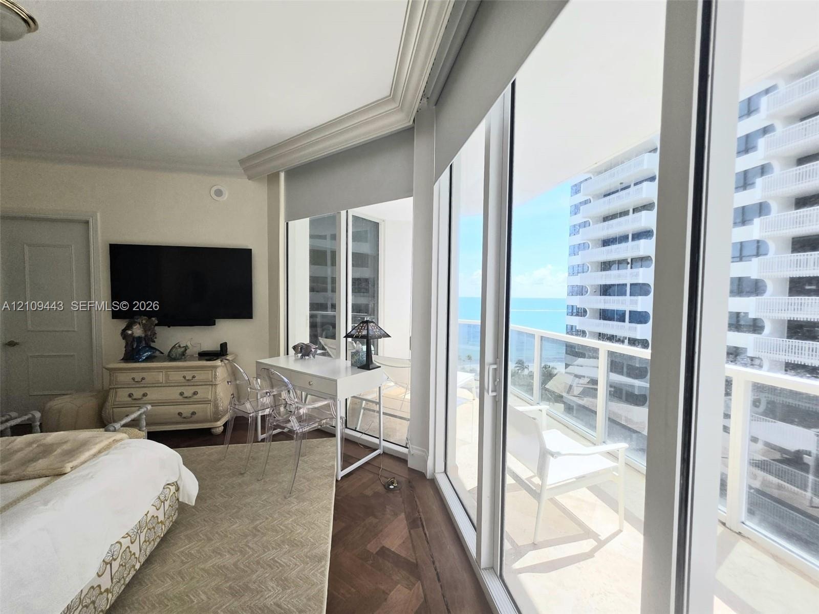 Floor-to-ceiling glass sliding doors, wood-finish flooring in a herringbone pattern, crown molding, and a private balcony featuring a glass panel rail