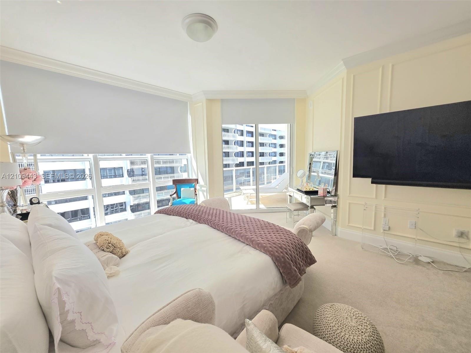 Expansive floor-to-ceiling windows, sliding glass door access to a private balcony, custom wall molding, neutral carpeting, and a ceiling-mounted ligh