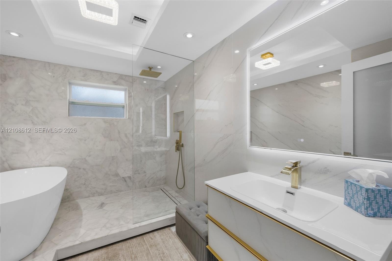 Bathroom featuring a freestanding soaking tub, a glass-enclosed shower with a rainfall showerhead, stone-patterned tile walls, a vanity with metallic 