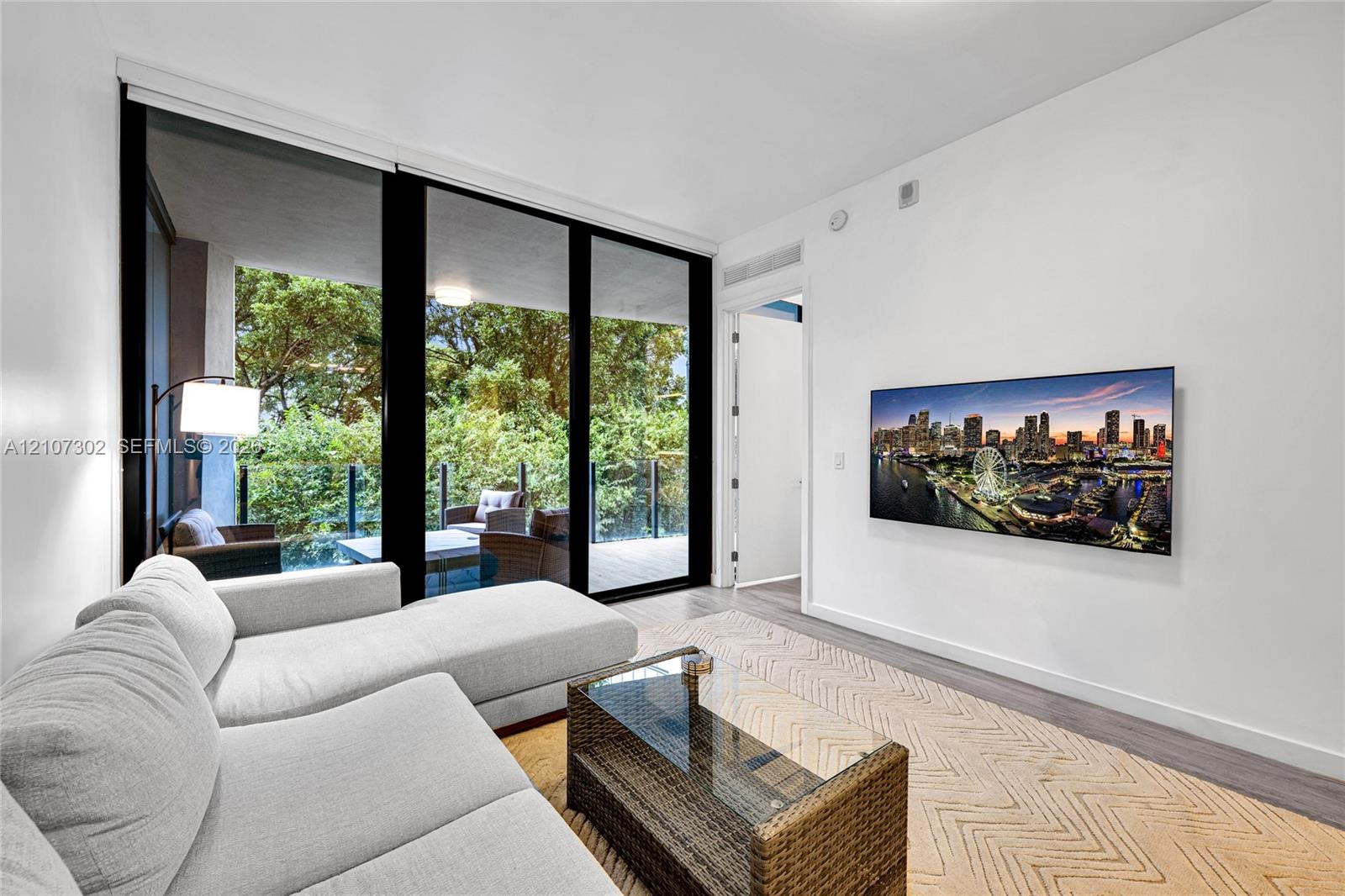 Floor-to-ceiling glass sliding doors, wood-finish flooring, and a private balcony with glass railing