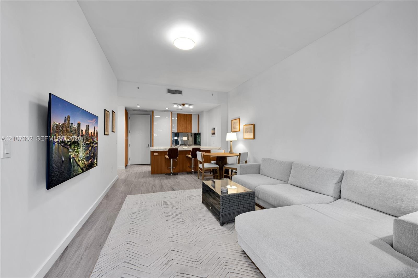 Open-concept living space featuring wood-finish flooring, recessed lighting, and kitchen cabinetry with a light stone countertop