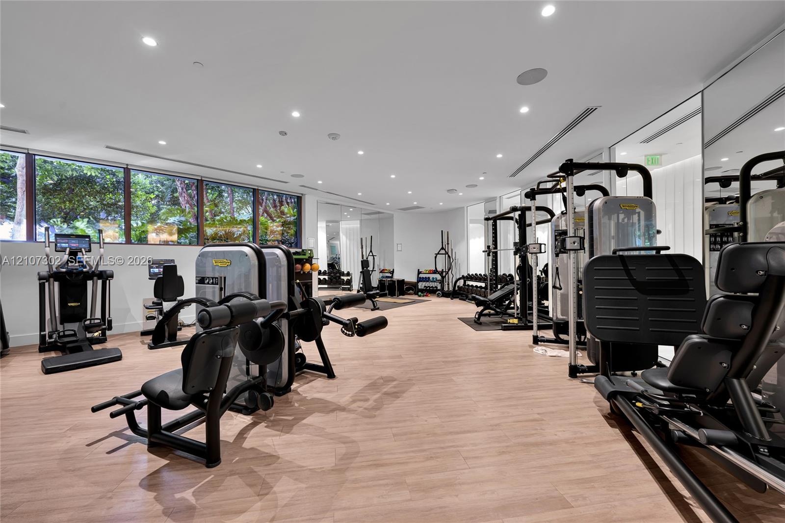 Fitness center featuring wood-finish flooring, extensive floor-to-ceiling mirrored walls, horizontal window banks, and recessed LED ceiling lighting