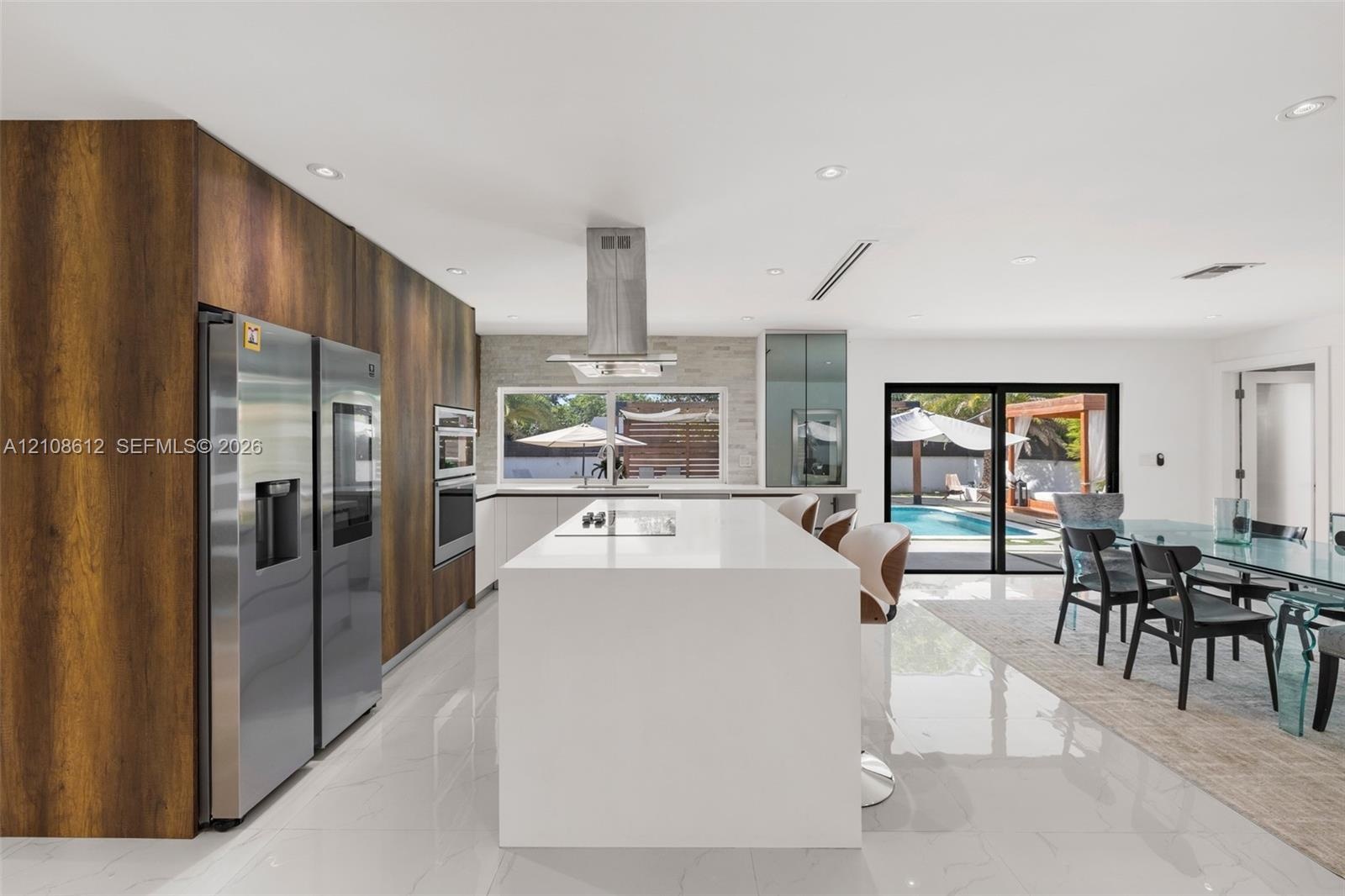 Modern kitchen featuring floor-to-ceiling wood-finish cabinetry, a white stone-surface island, stainless steel built-in appliances, recessed lighting,