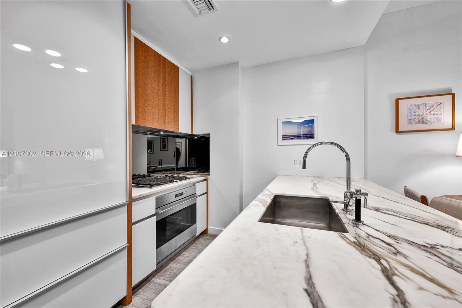Contemporary kitchen featuring white high-gloss cabinetry, stone-surface countertops, an undermount sink with a gooseneck faucet, stainless steel wall