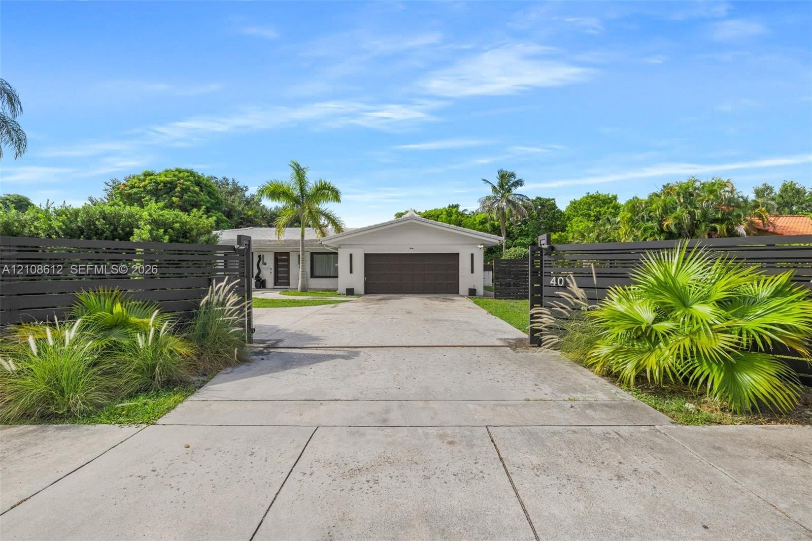 Single-story residence featuring a two-car garage, concrete driveway, horizontal slat fencing, and mature landscaping