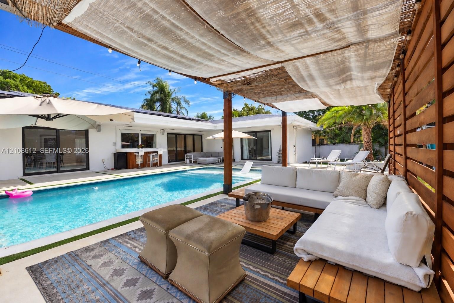 Outdoor patio area featuring a slatted wood privacy wall and an overhead woven fabric canopy, including a rectangular swimming pool surrounded by a co