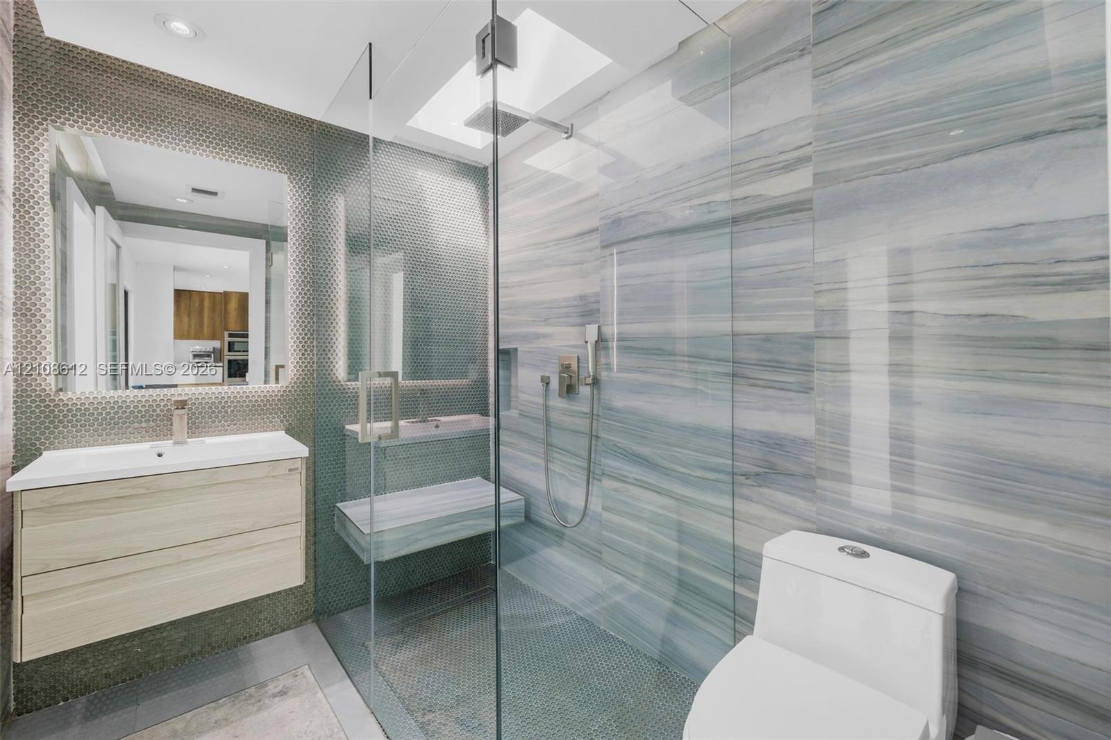 Floating wood-finish vanity with a rectangular sink, walk-in glass-enclosed shower featuring stone-finish wall tile, built-in stone-finish shower benc