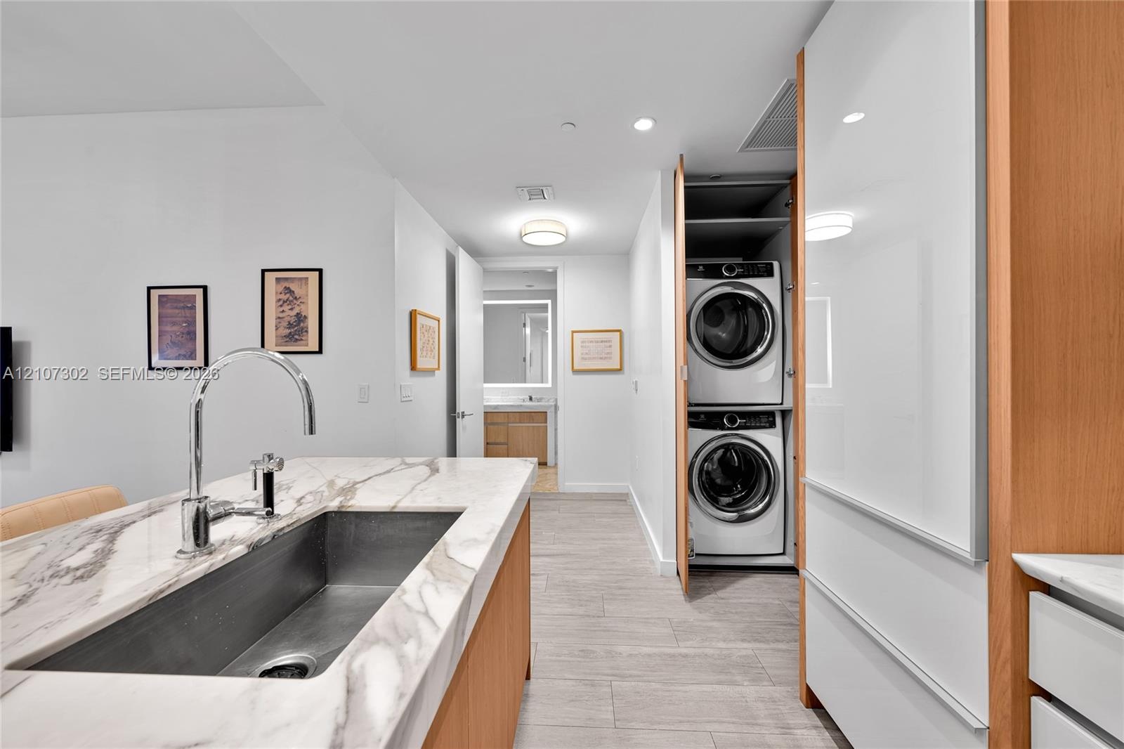 Kitchen island with stone countertop, stainless steel undermount sink, high-arc faucet, wood-finish cabinetry, and built-in laundry closet with stacke