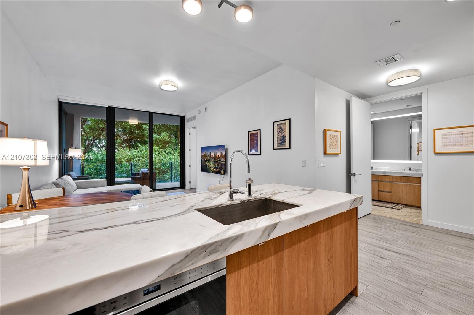 Kitchen island with stone countertop, undermount sink, gooseneck faucet, light wood-finish cabinetry, and wood-finish tile flooring