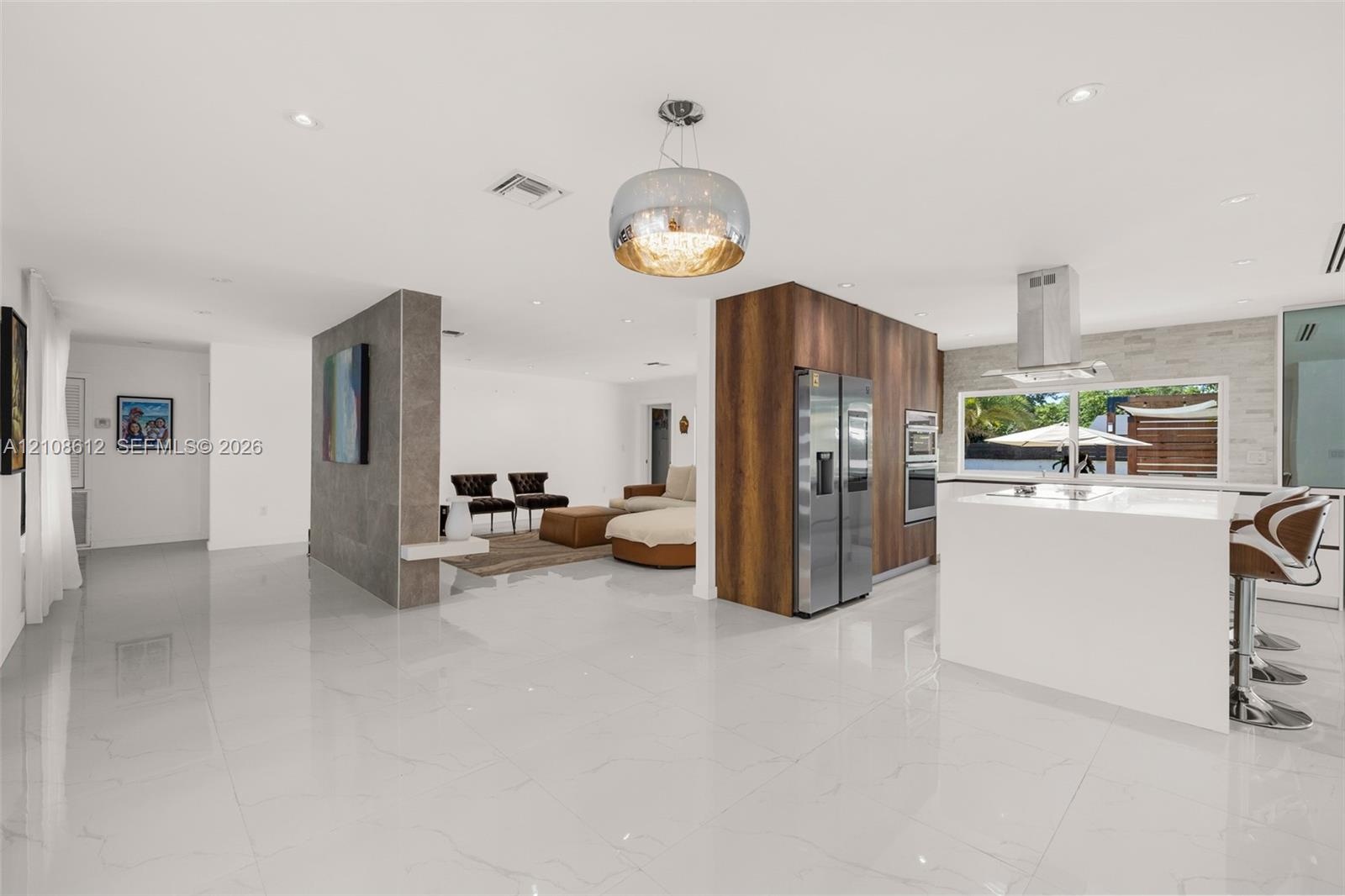 Open-concept interior featuring large-format tile flooring, a central wood-finish cabinetry partition with integrated stainless steel appliances, a ki