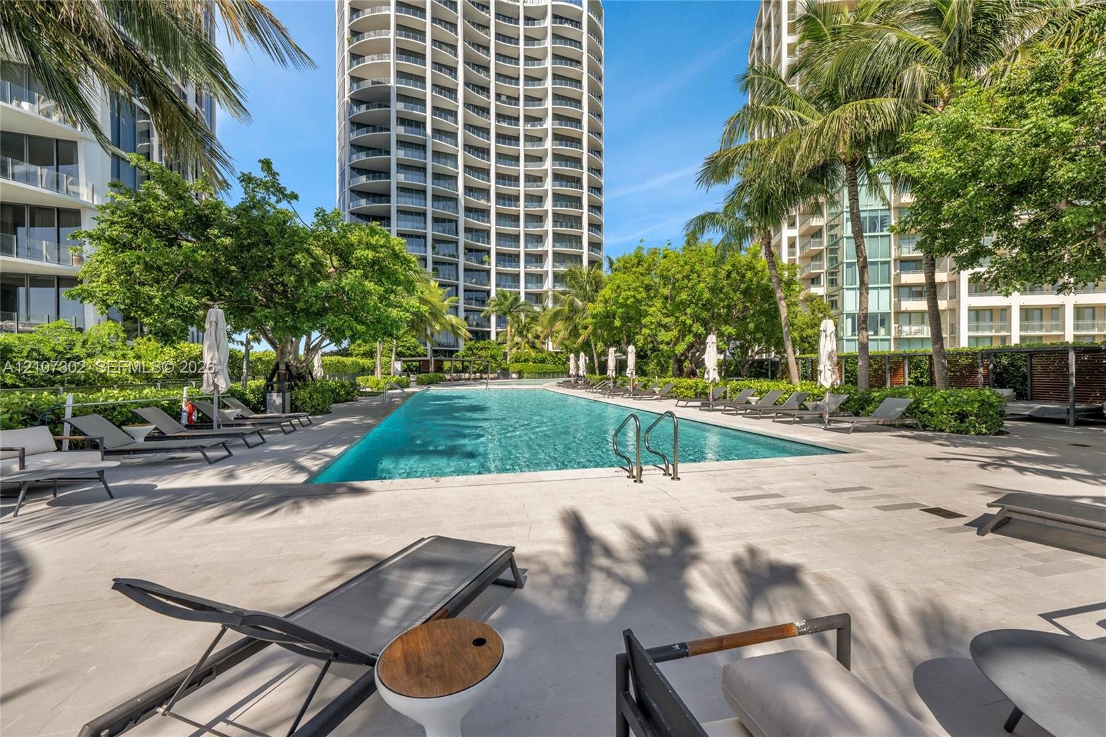Swimming pool featuring stone pavers, metal pool ladder, and palm tree landscaping