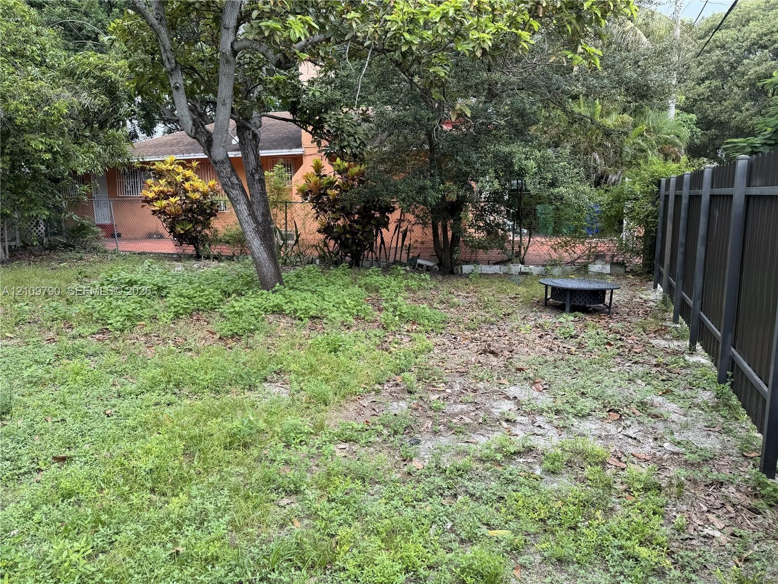 Backyard area featuring mature trees, peripheral landscaping, and a vertical metal privacy fence